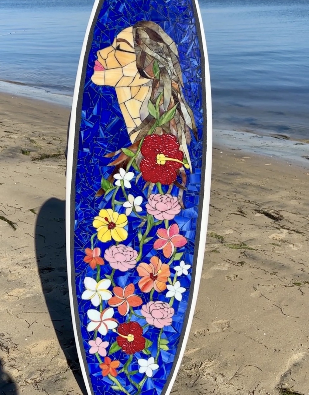 stained glass mosaic art surfboard with woman's face looking up and flowers intertwined in her hair